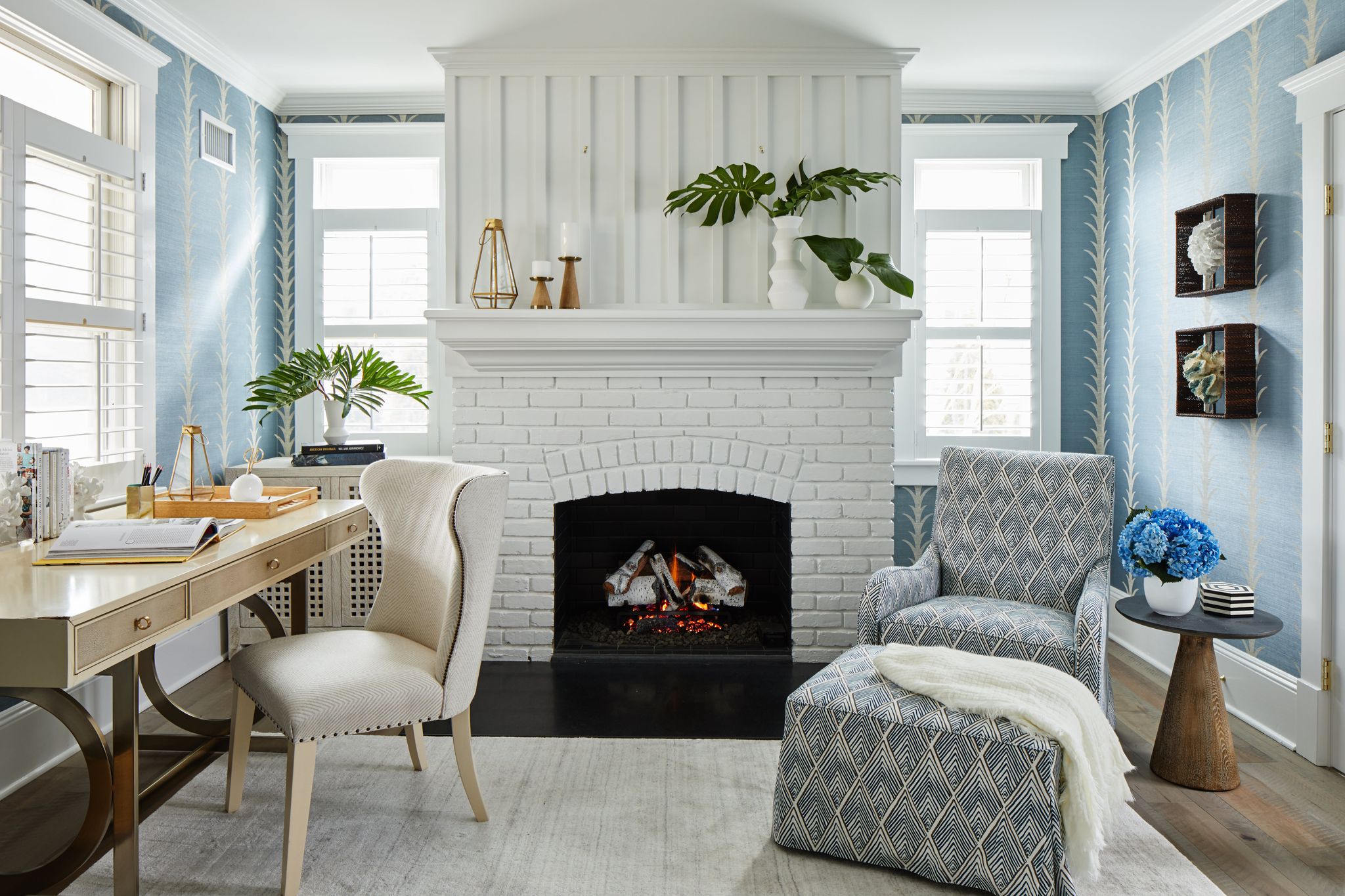 a coastal office with blue patterned wallpaper and a white brick fireplace