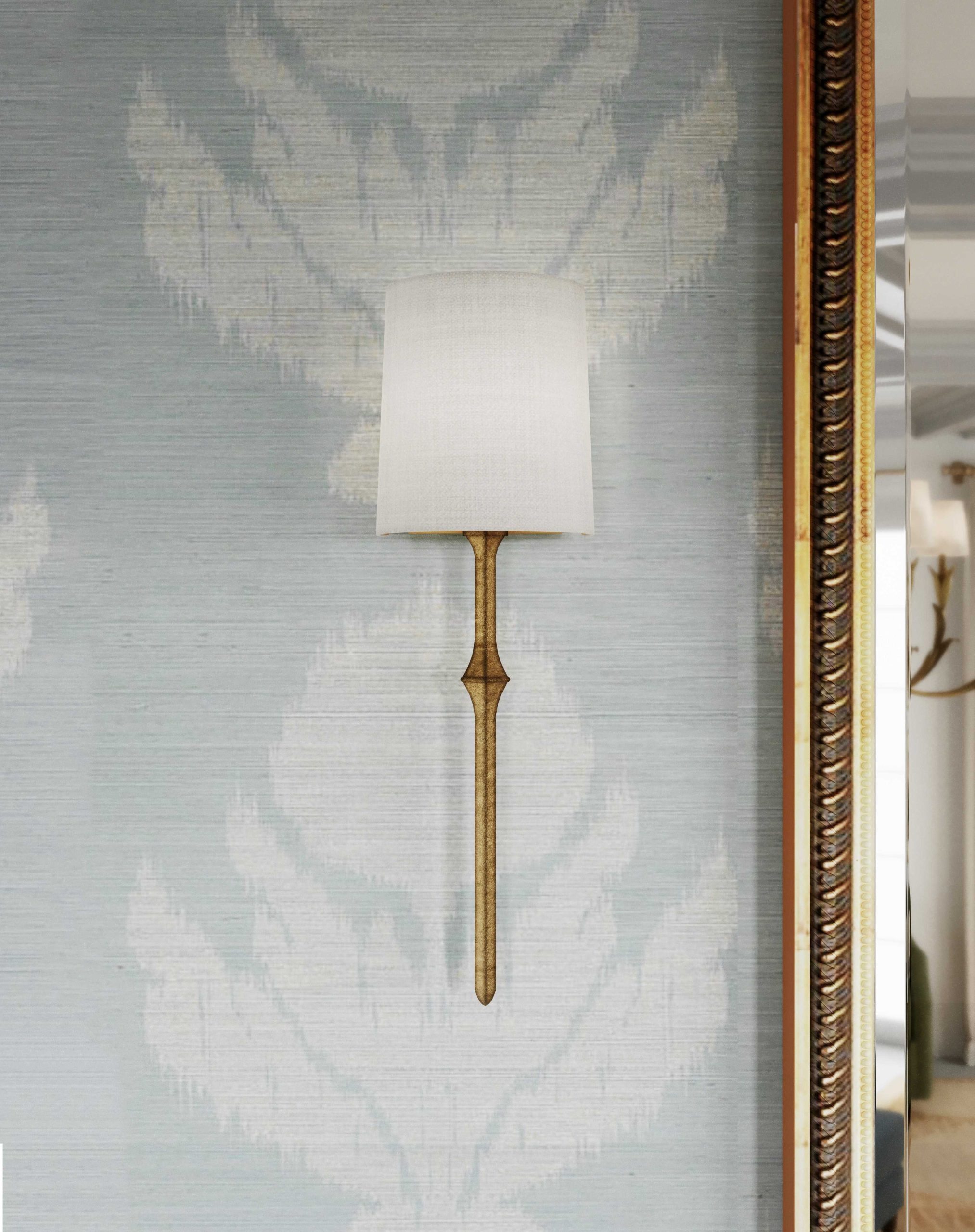 An antique gold sconce with a white shade with blue and white wallpaper behind it