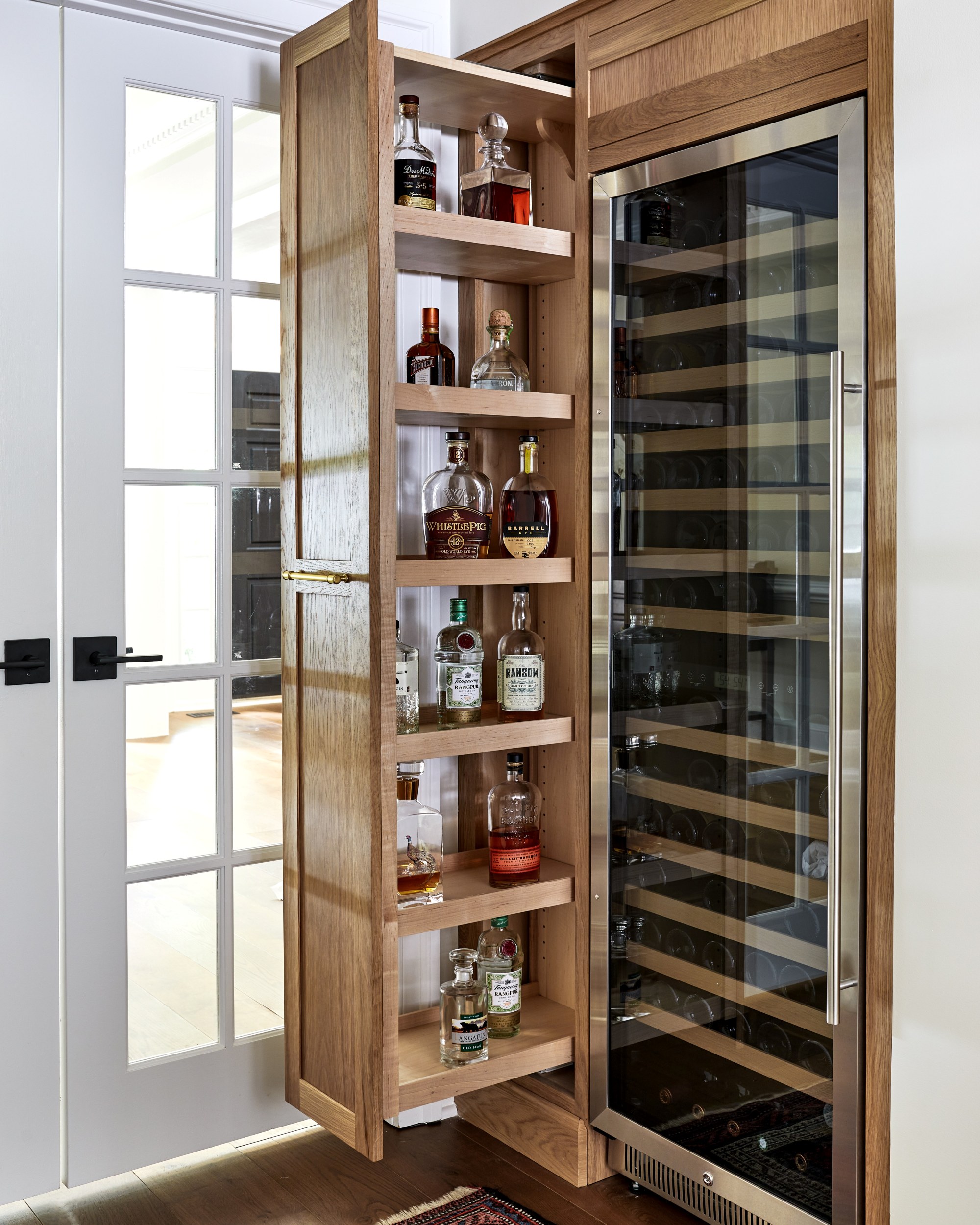 A custom pull-out pantry in a kitchen next to a tall glass front wine fridge